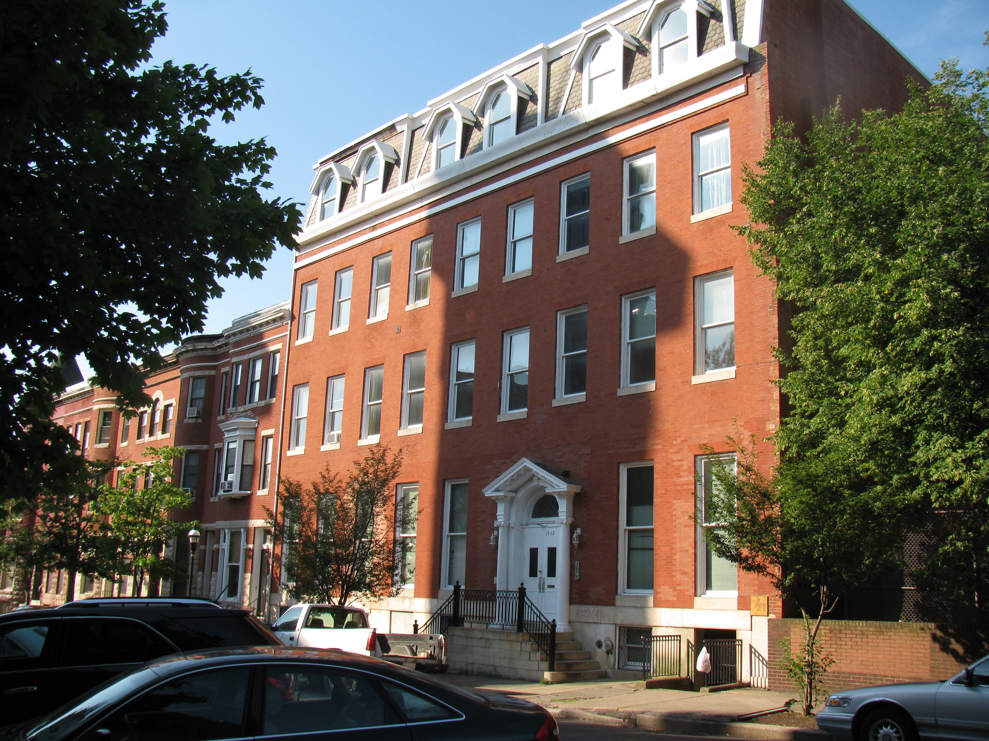 The 4 story building is clad in red brick and has a mansard roof.