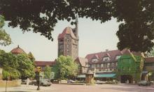 A photographic postcard of a low red teracotta roof building with a tower in the center